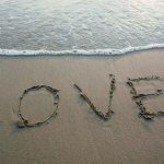 Love written in sand with ocean waves at the beach, evoking romance and tranquility.
